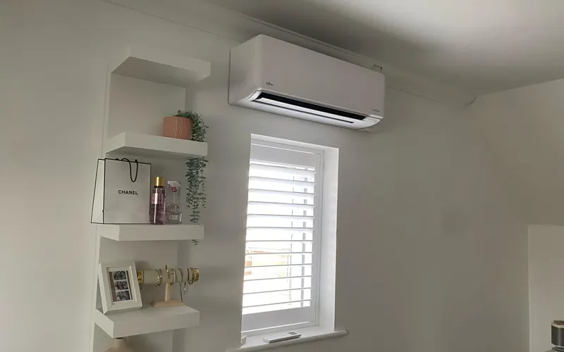 Wall-mounted home air conditioning unit above a window in a finished room