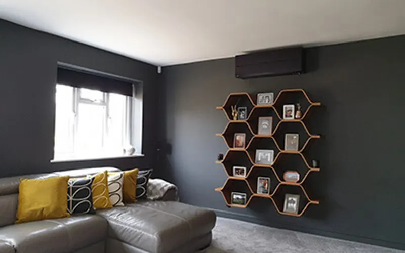 Slim wall-mounted indoor unit above a sofa in a house living room (residential case study)