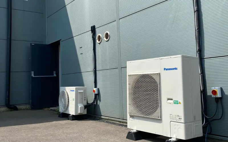 Panasonic outdoor units on a paved yard against a grey clad building
