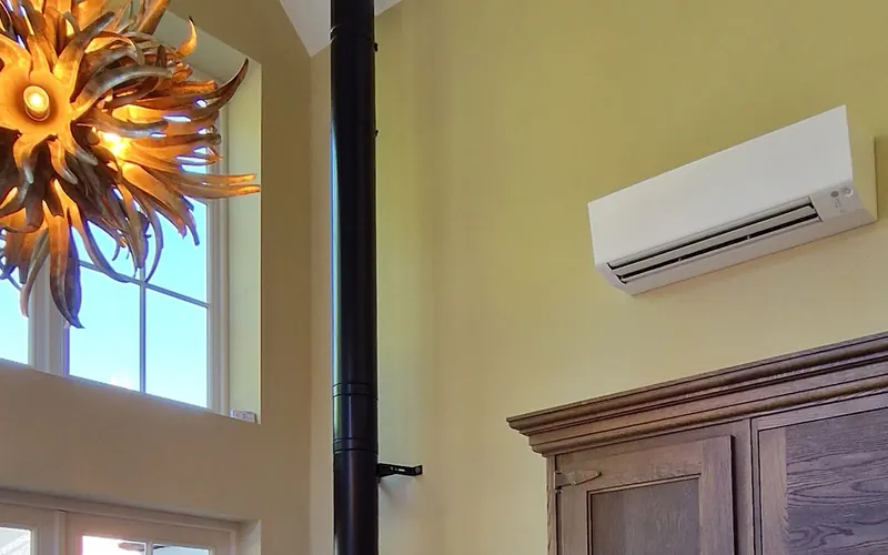 Wall-mounted indoor unit fitted high on a wall beside a tall window in a finished room