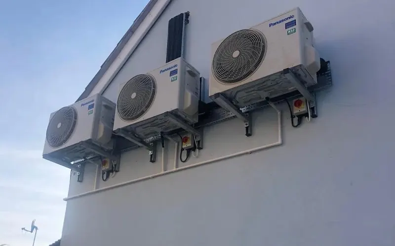 Three Panasonic outdoor air conditioning units on the side of a house