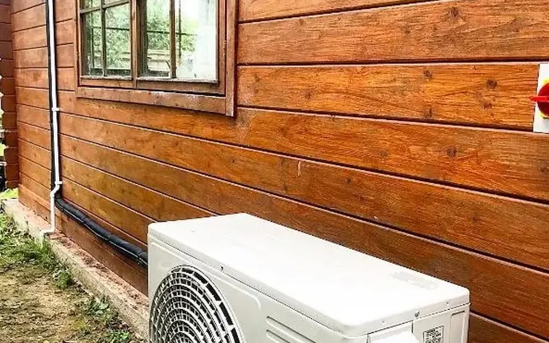 Air conditioner outdoor unit outside a wood panelled house