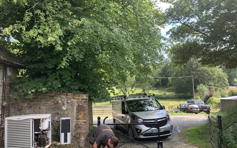 Outdoor unit being installed beside a stone wall, with the company van